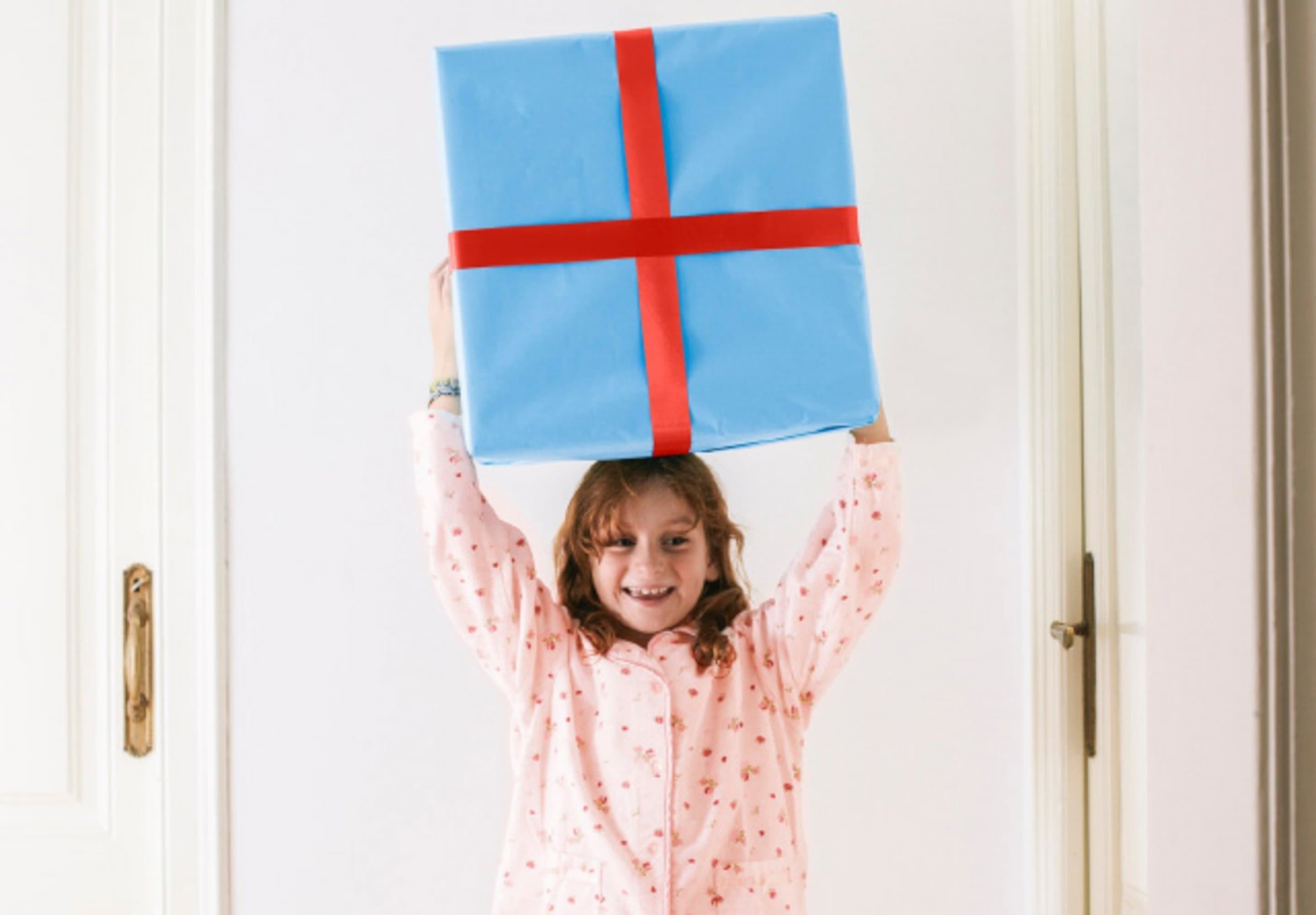 Kleines Mädchen hält ein großes Geschenk in die Luft.