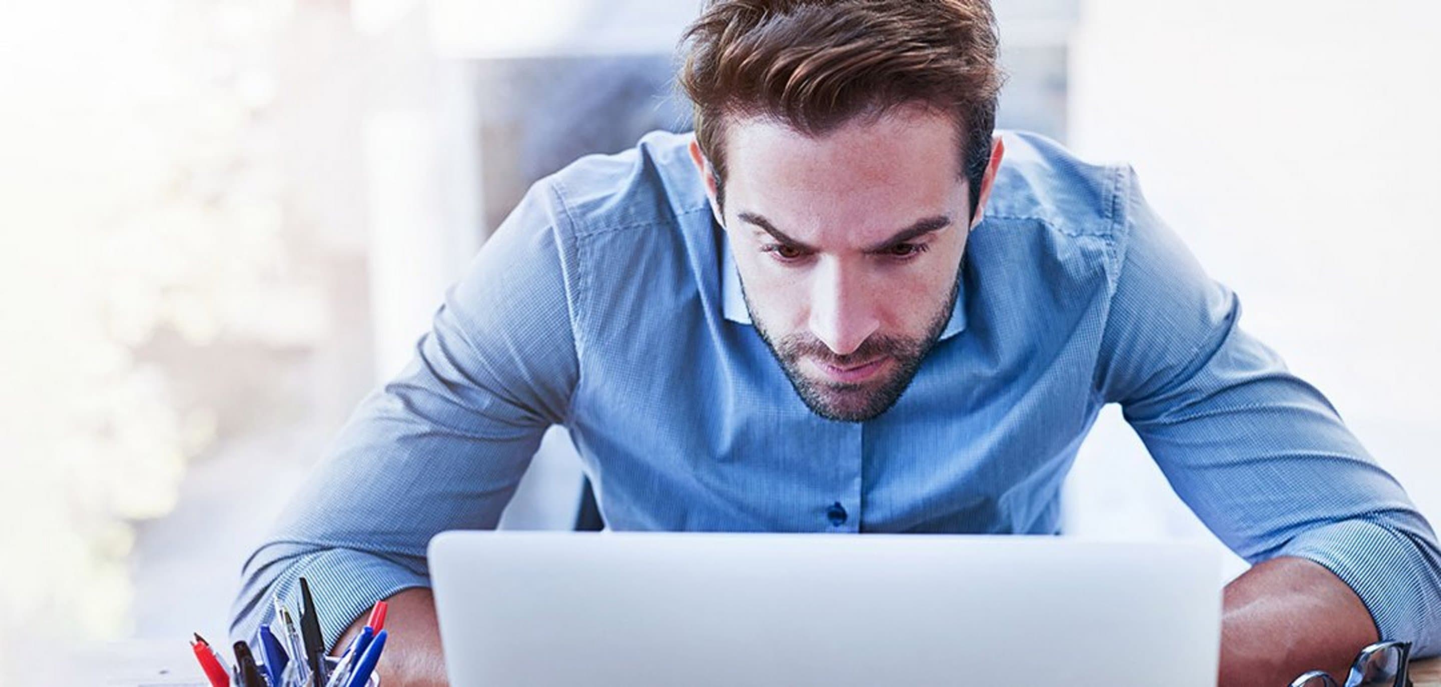 Mann sitzt vorgebeugt vor einem Laptop und schaut angestrengt auf diesen.