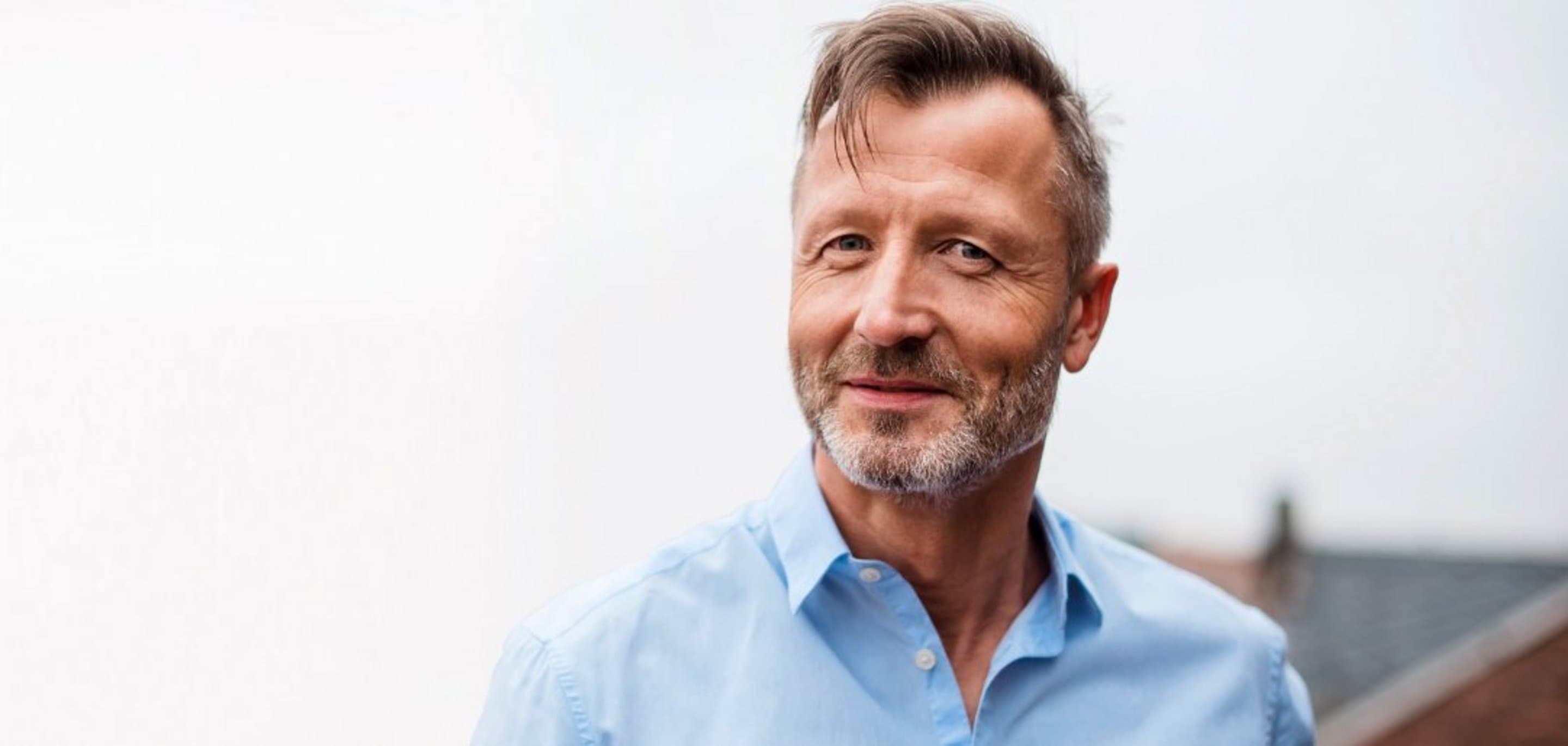 Portrait von Mans mit blauem Hemd, der in die Kamera lächelt.