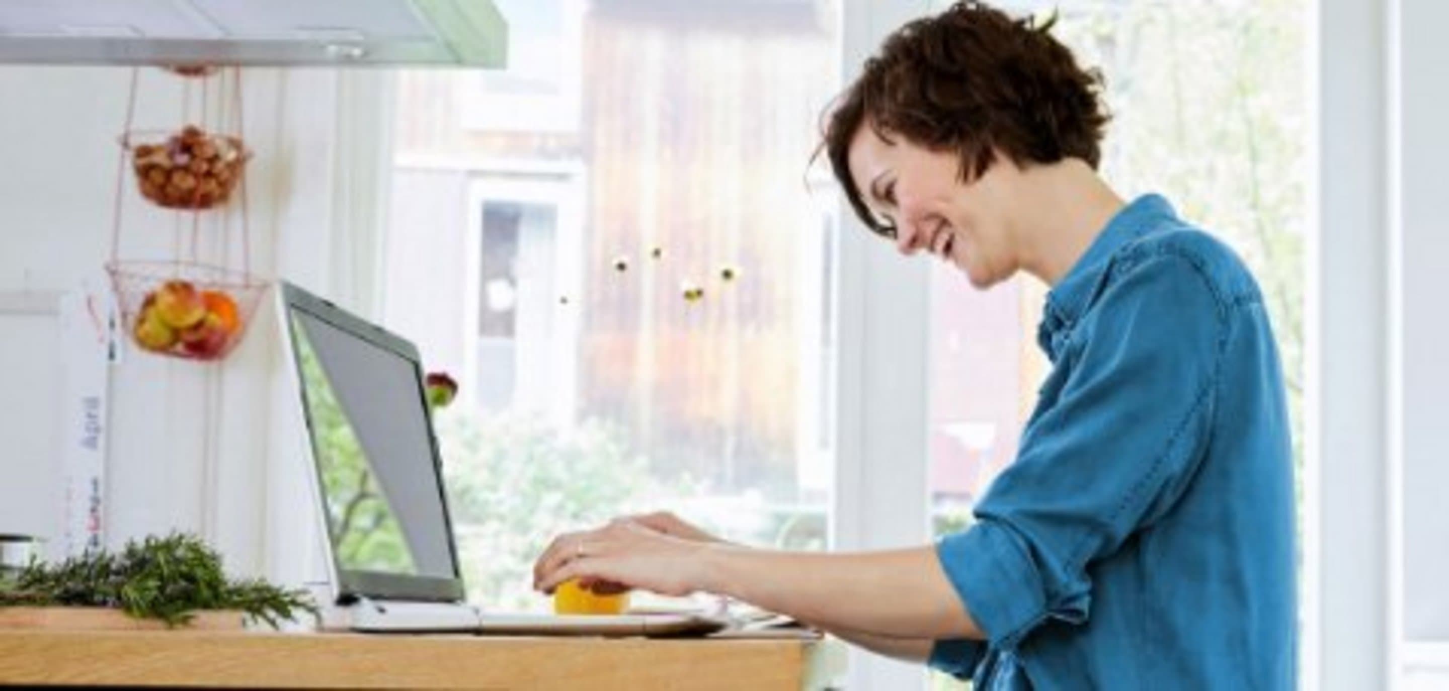 Frau sitzt lachend am Schreibtisch vor einem Laptop.