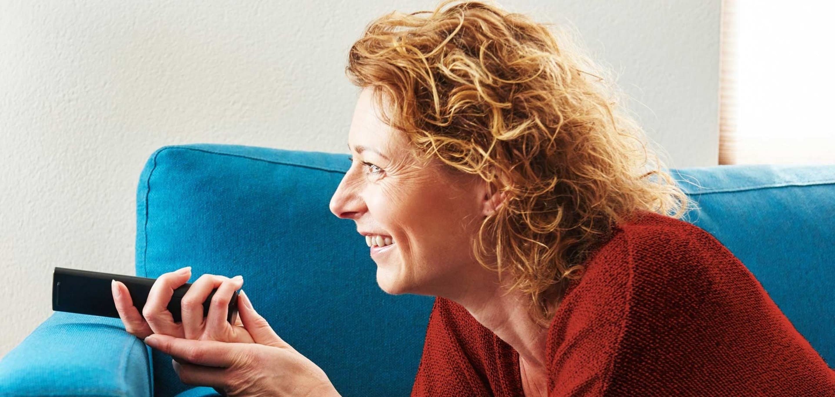 Frau liegt auf der Couch und hält Fernbedienung in der Hand