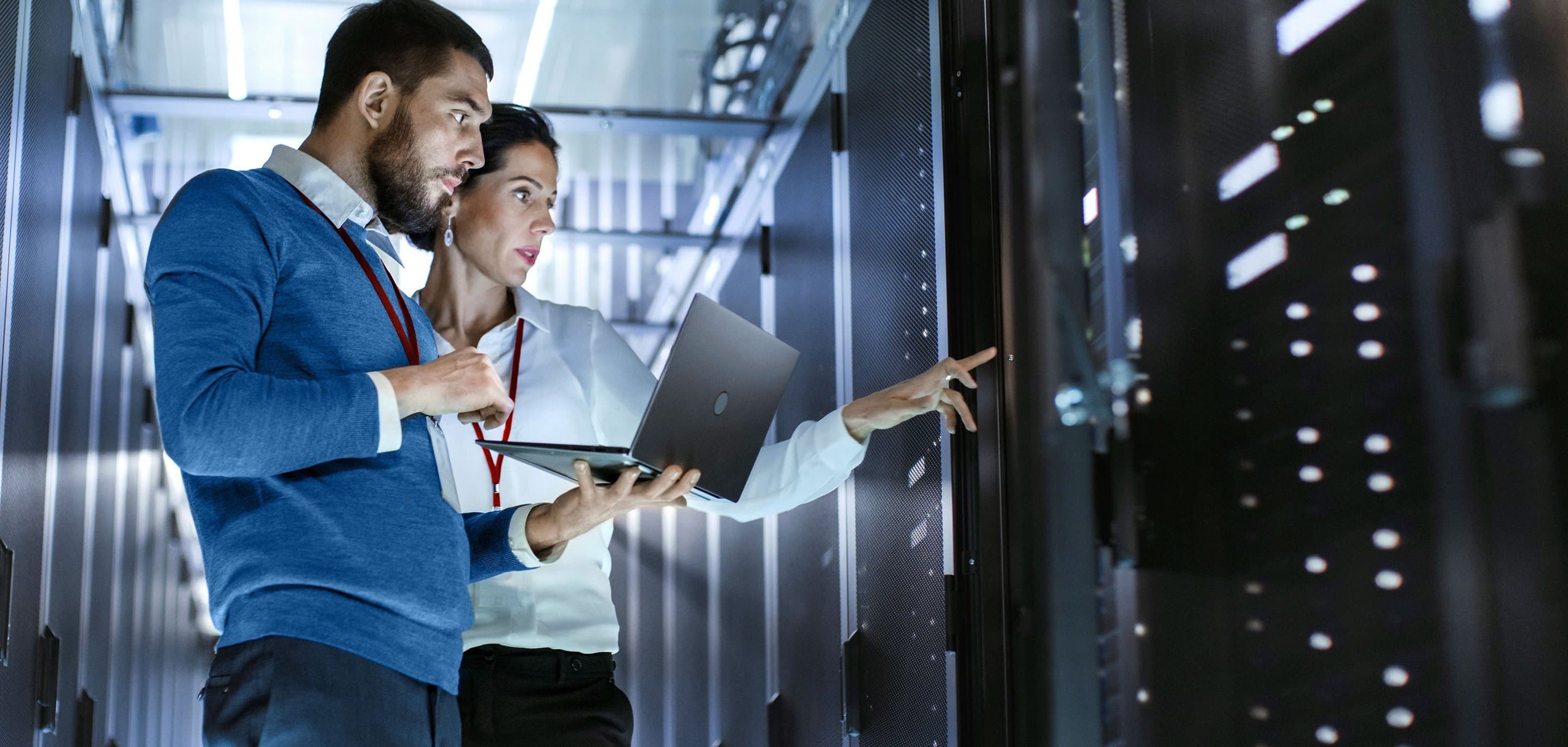Serverraum Zwei Personen im Serverraum, eine mit Laptop, die andere zeigt auf ein Serverrack.