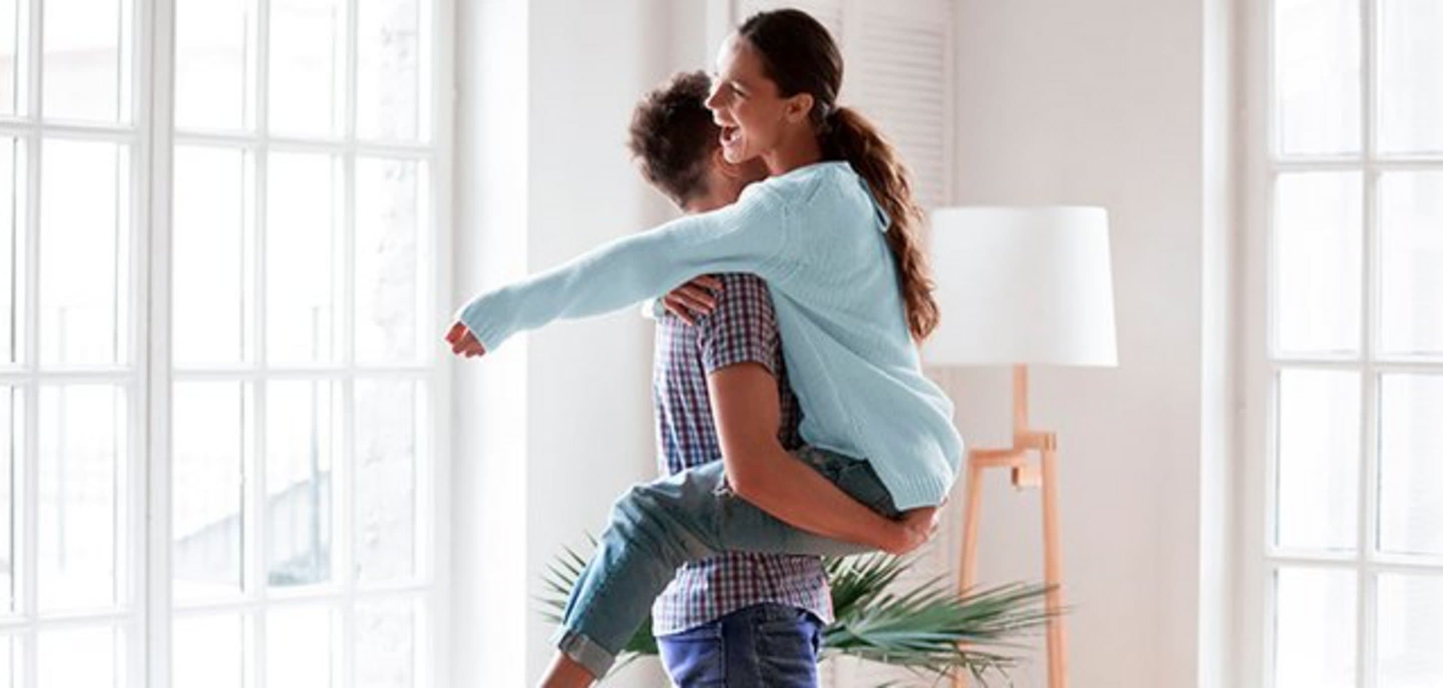 Ein Mann hebt eine Frau im Wohnzimmer hoch und lachen dabei