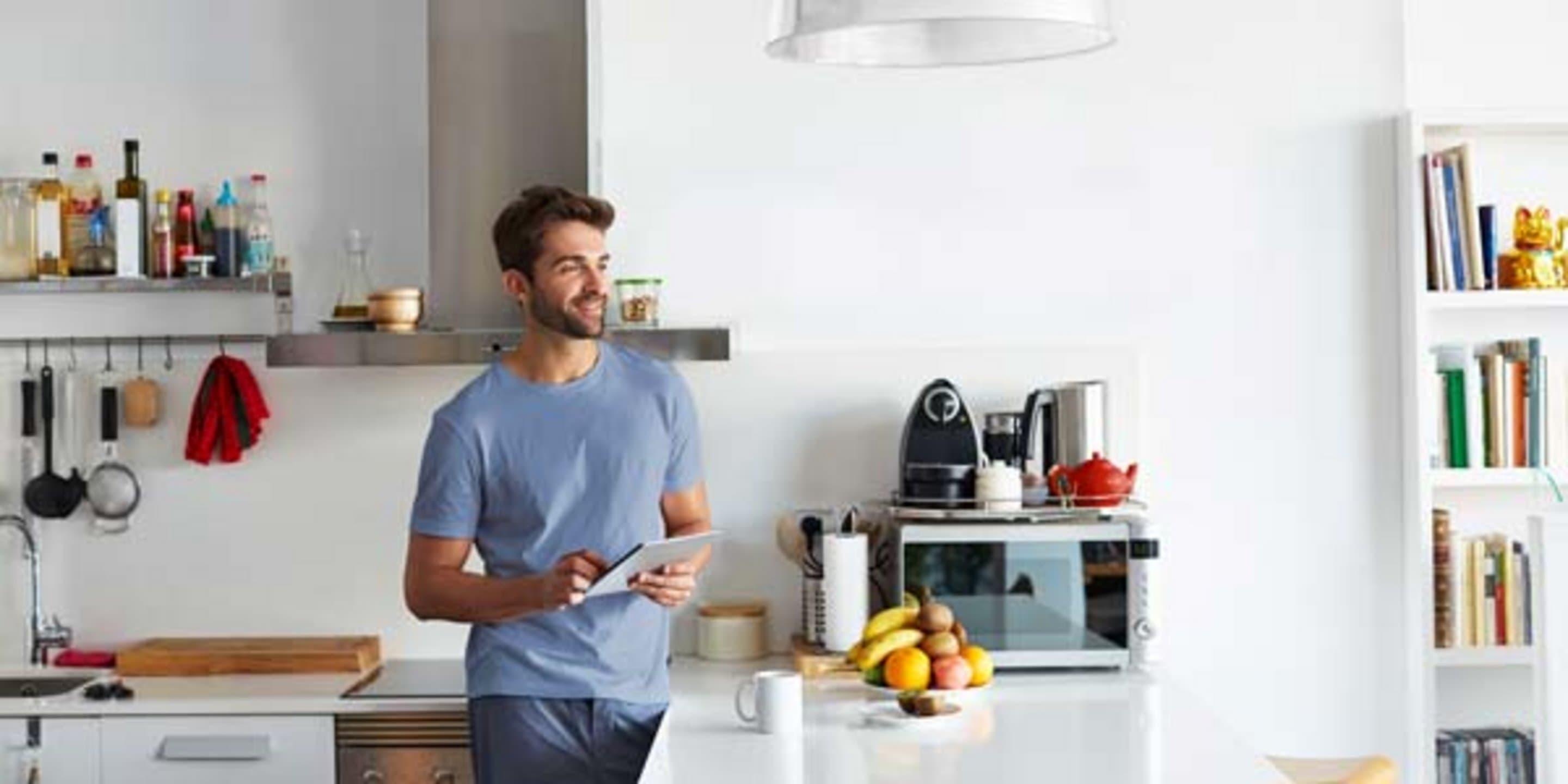 Mann steht in einer Küche, lächelt und hält ein Tablet in der Hand.