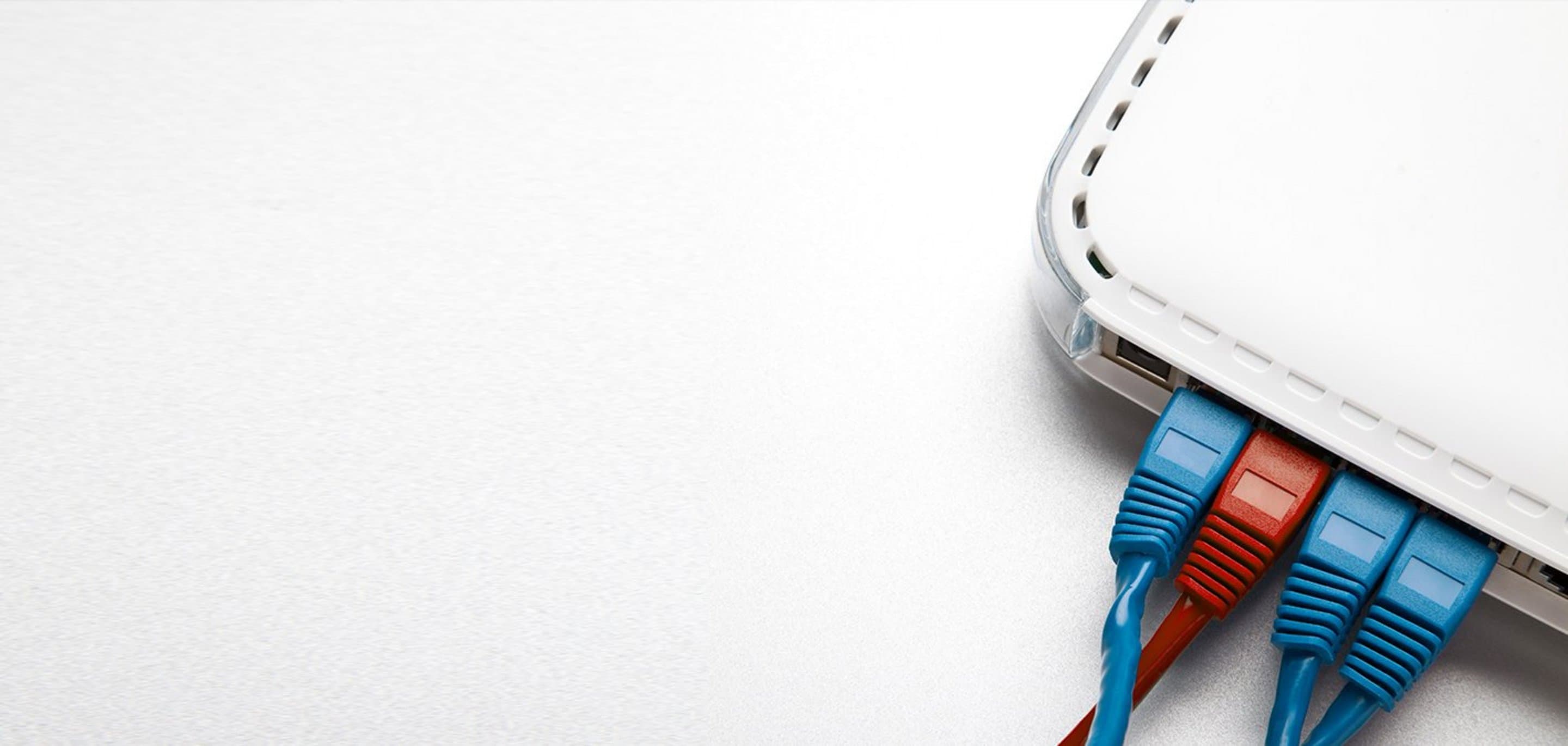 Grauer Hintergrund auf dem in der Ecke ein Teil eines Routers zu sehen ist, in dem blaue und rote Kabel stecken.
