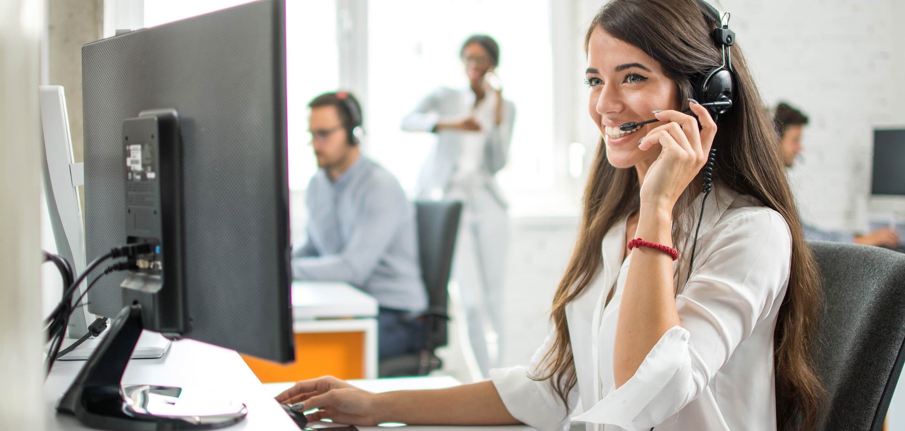 Symbolbild für Hosted PBX Eine junge Frau sitzt am Desktop und telefoniert per Headset.