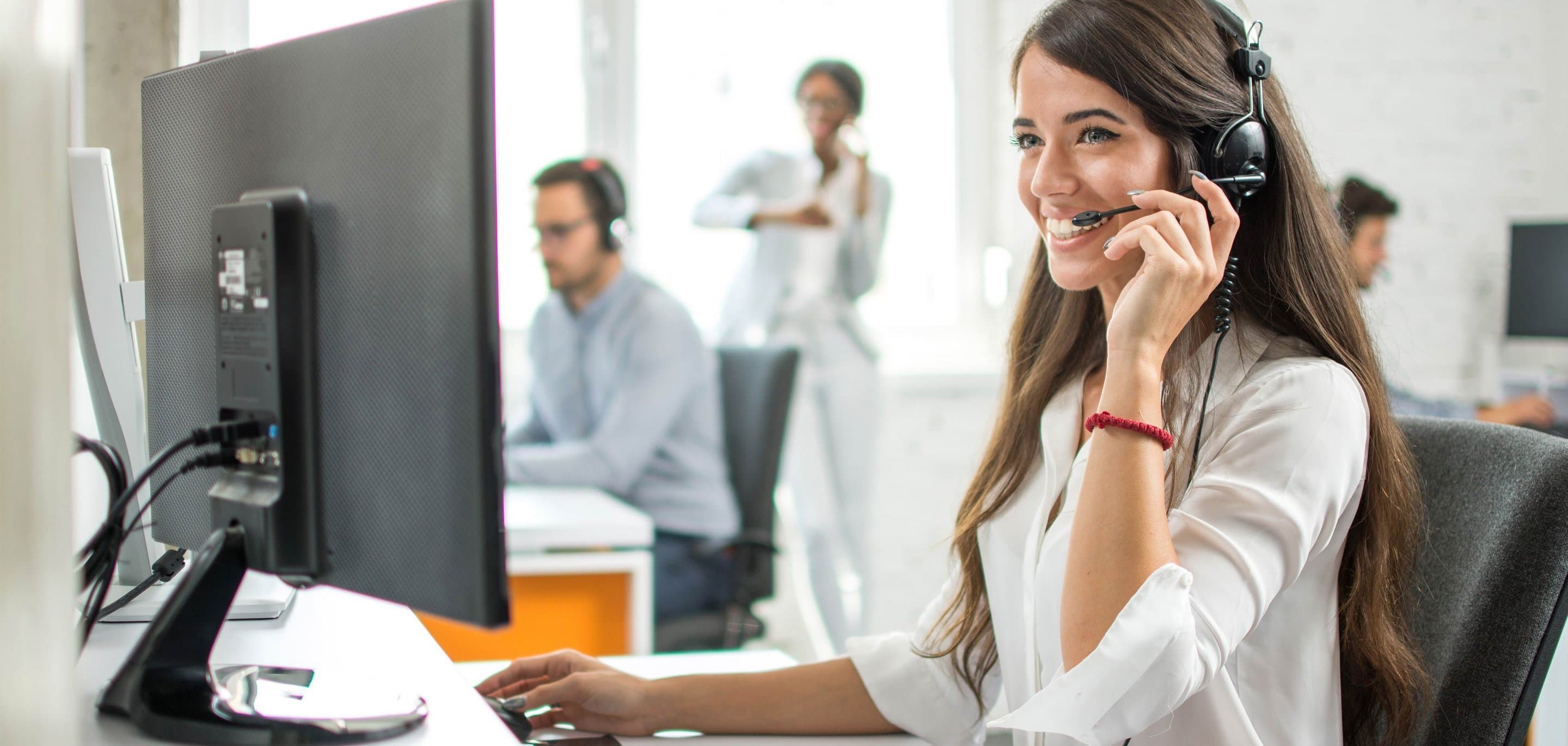 Symbolbild für Hosted PBX Eine junge Frau sitzt am Desktop und telefoniert per Headset.