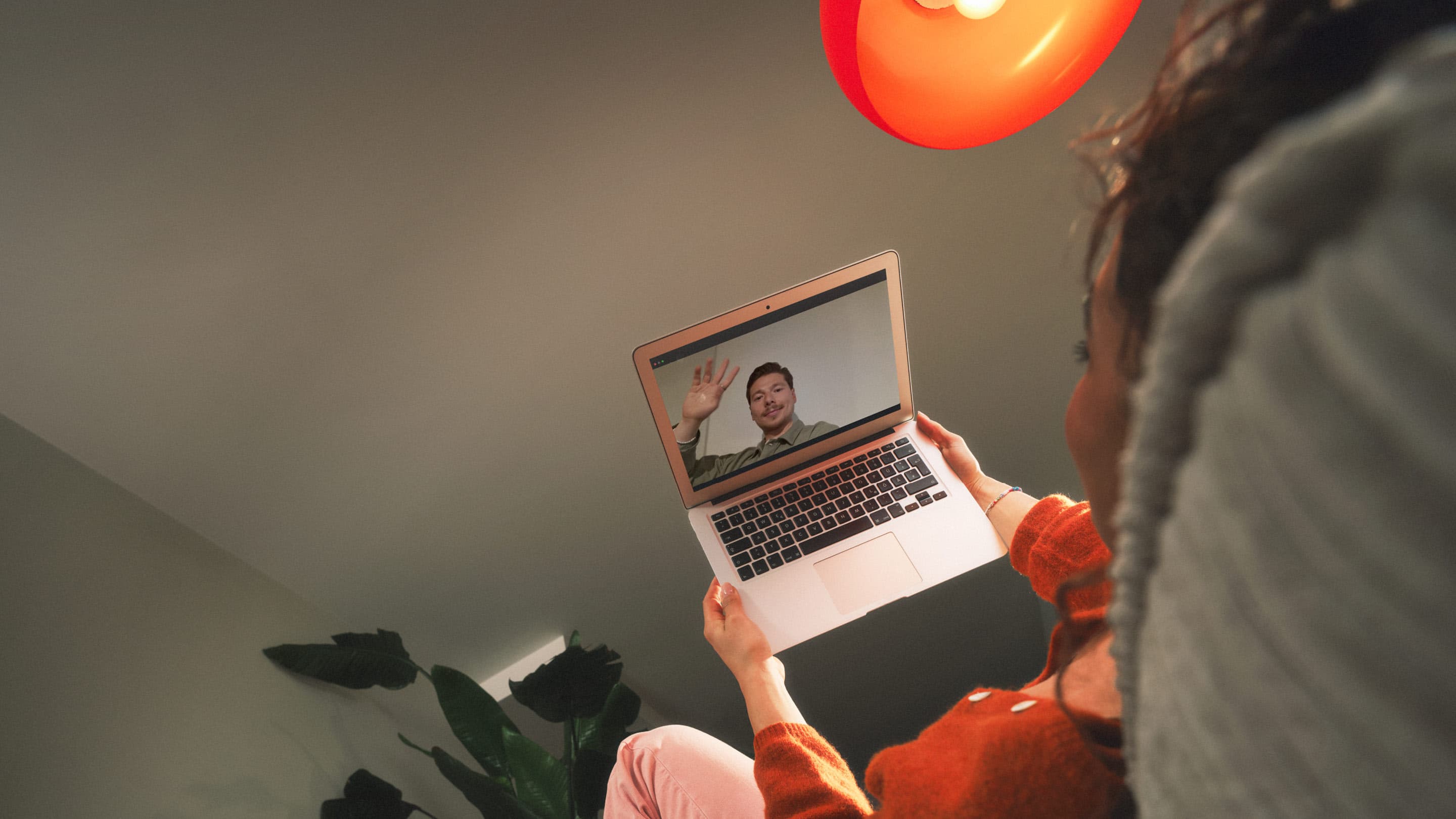 Eine Person hält einen geöffneten Laptop und führt einen Videocall, bei dem auf dem Bildschirm eine weitere Person zu sehen ist.