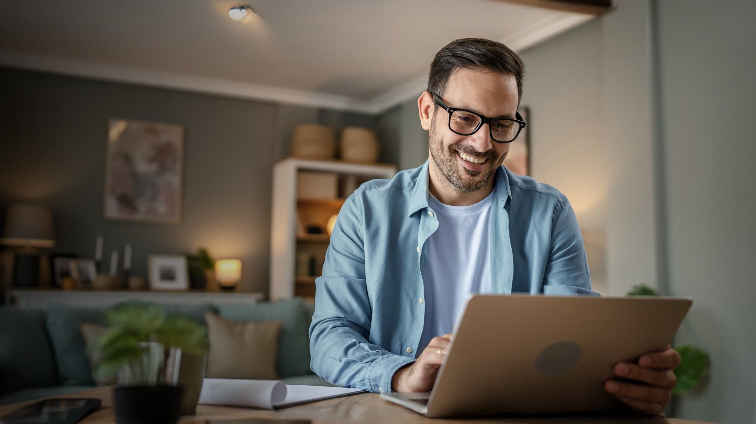 Mann sitzt am Tisch vor aufgeklapptem Laptop