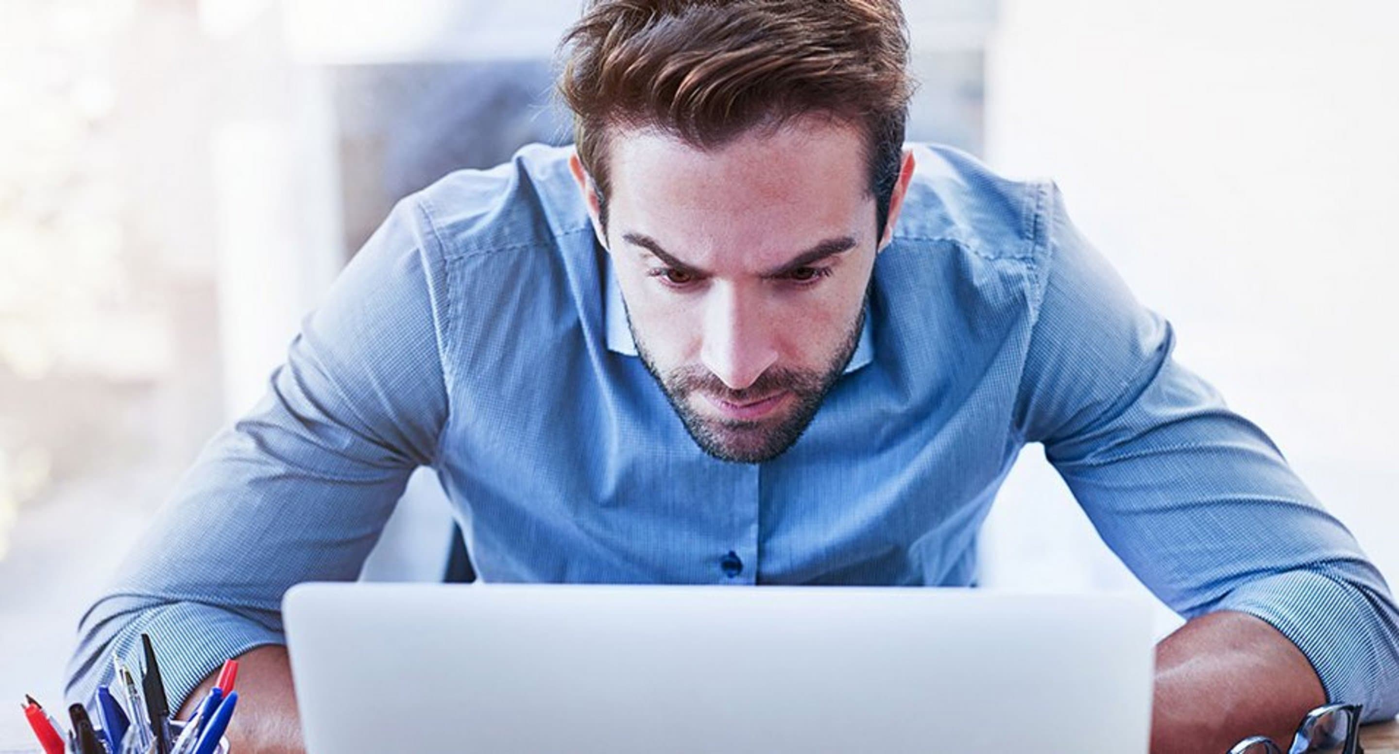 Mann sitzt vorgebeugt vor einem Laptop und schaut angestrengt auf diesen.