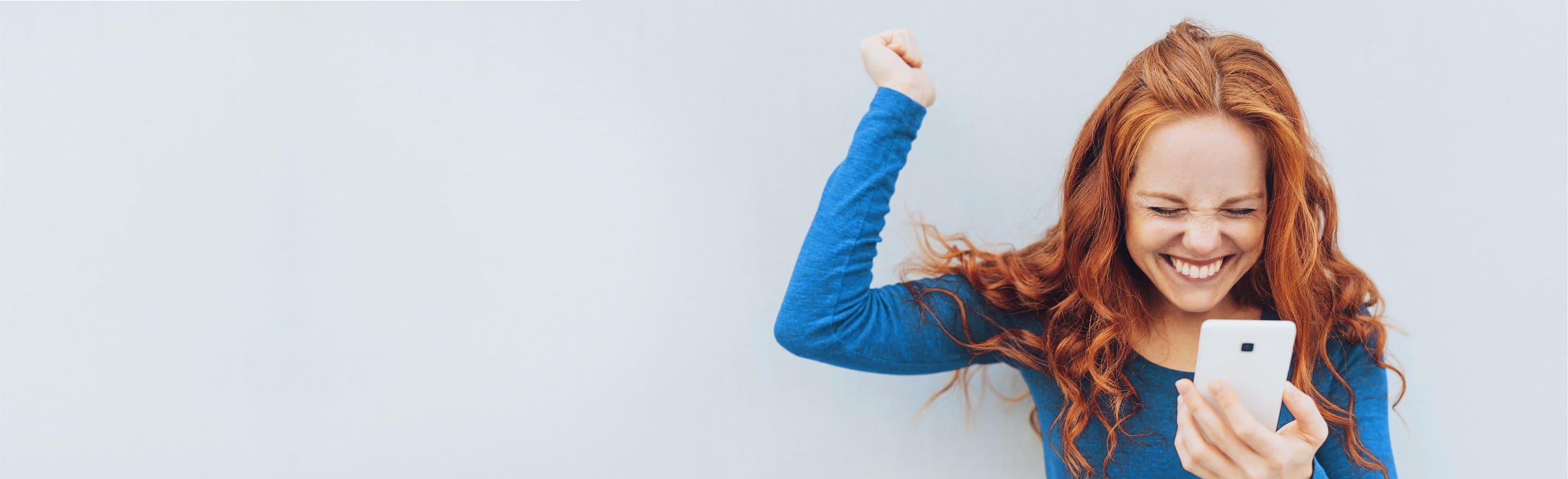 Junge Frau schaut auf ihr Handy und freut sich