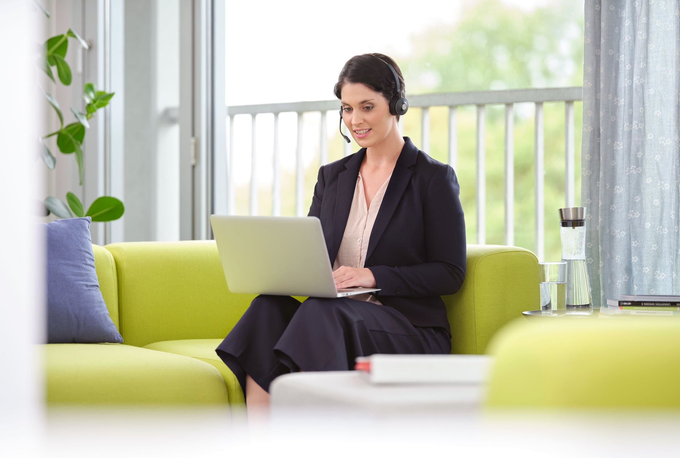 Frau mit Headset Frau mit Laptop und Headset sitzt auf grünem Sofa.