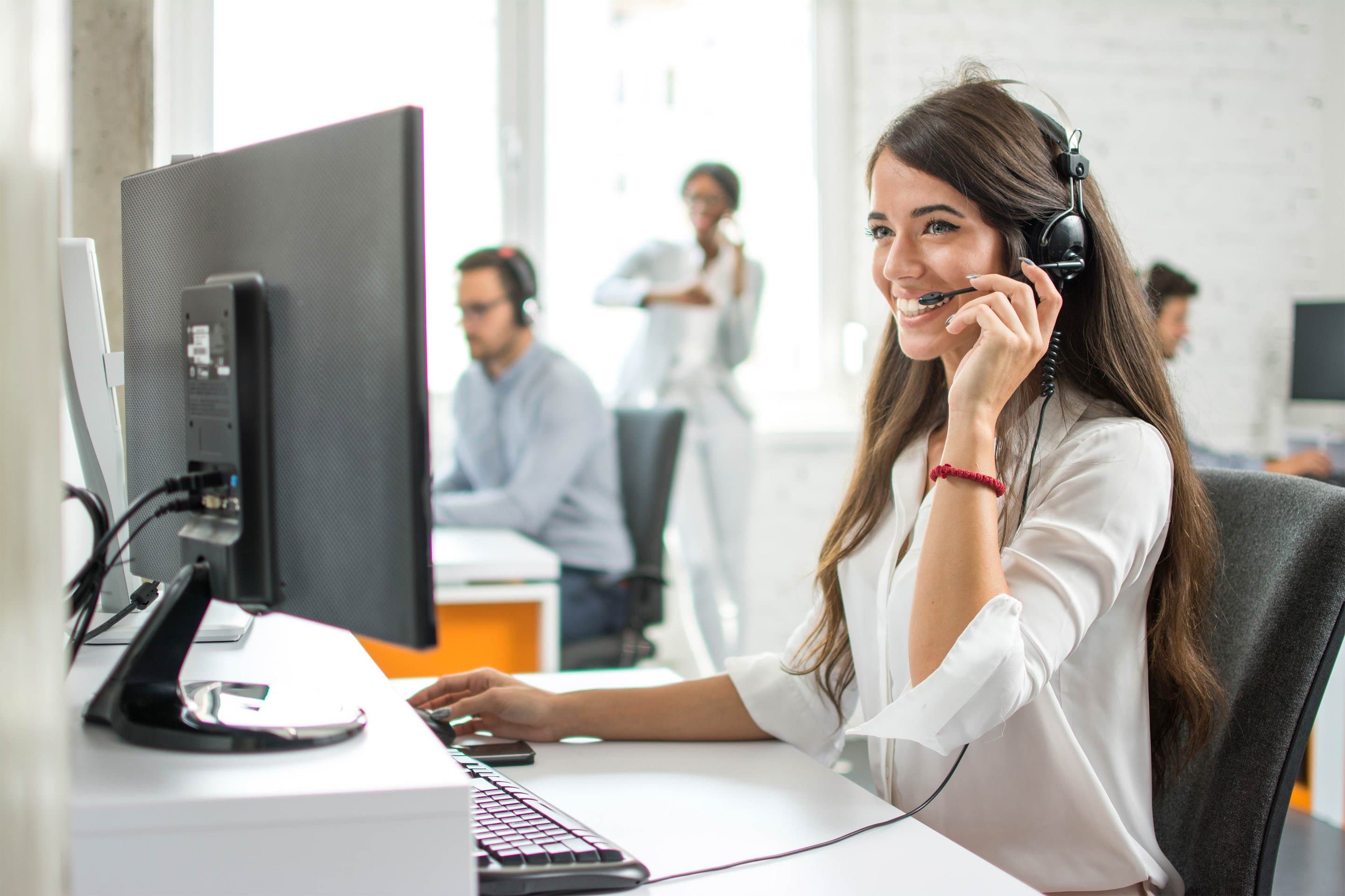 Symbolbild für Hosted PBX Junge Frau mit Headset sitzt telefonierend an einem Desktoprechner in einem Büro.